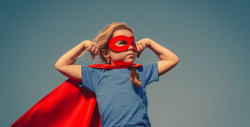 Funny little power super hero child (girl) in a red raincoat. Superhero concept. Instagram colors toning